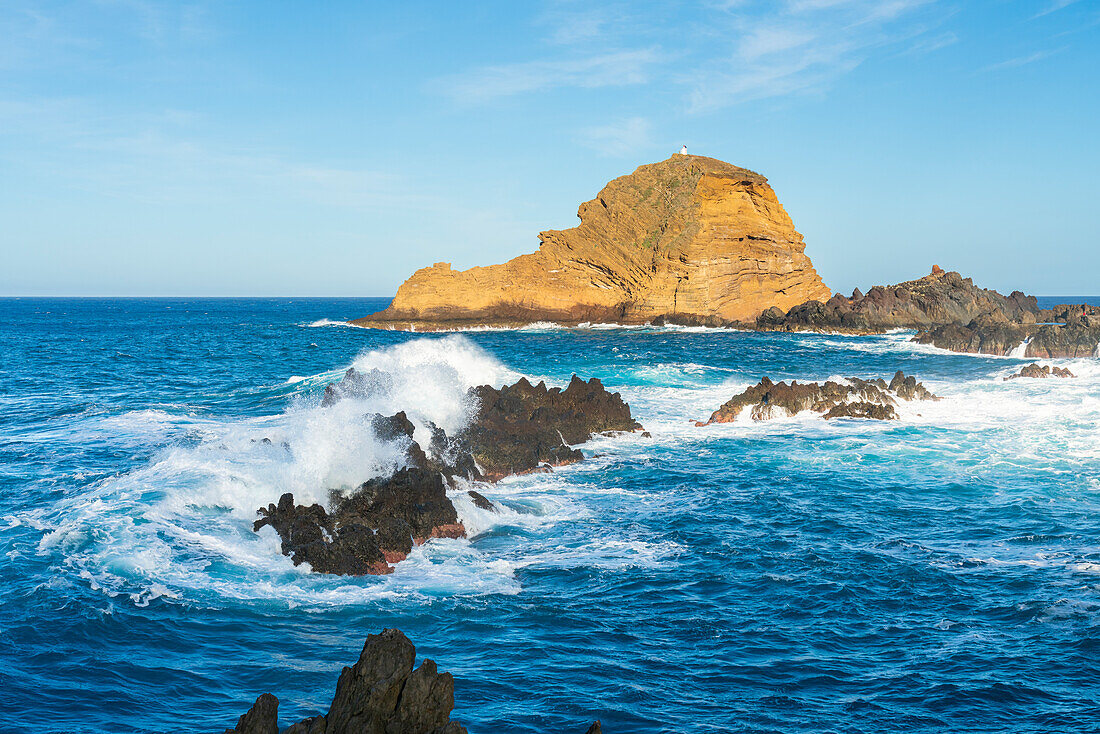 Waves washing rock formation near coast of Porto Moniz and distant view of lighthouse on Ilheu Mole Island, Madeira, Portugal, Atlantic, Europe