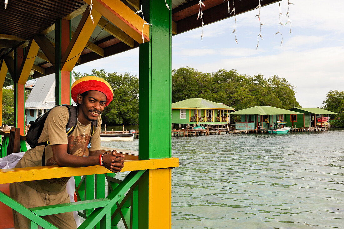 Mann lehnt sich an das Geländer eines Stelzenhauses in Cayo Coral, südliche Landzunge der Insel Bastimentos, Bocas del Toro Archipel, Republik Panama, Mittelamerika