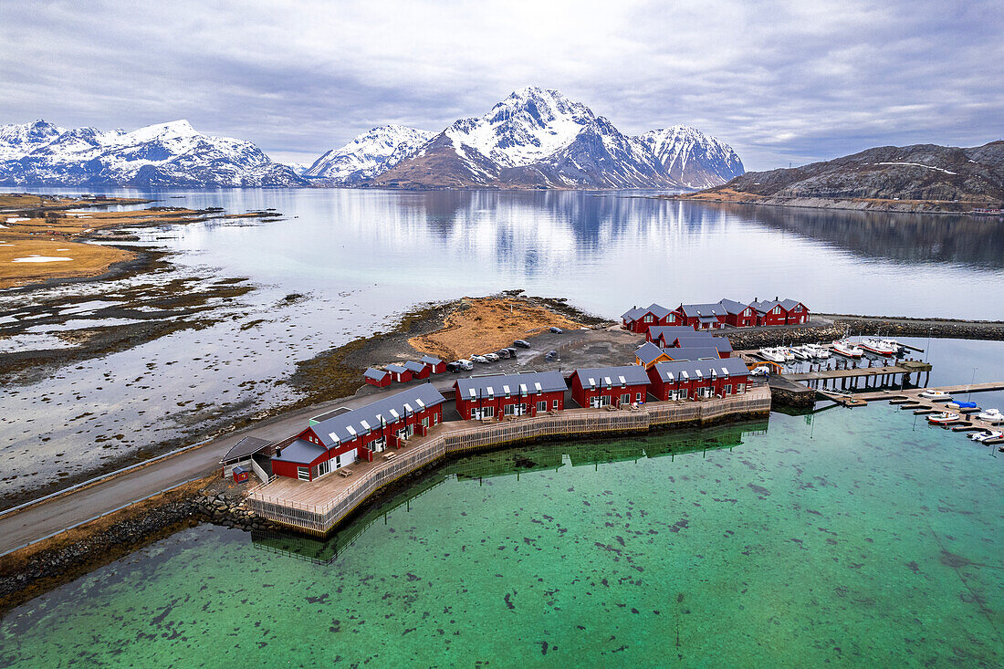 Luftaufnahme der traditionellen roten Rorbu umgeben von majestätischen, schneebedeckten Bergen, Vestvagoy, Lofoten, Norwegen, Skandinavien, Europa