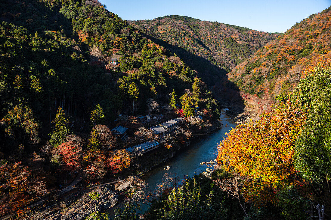 Autumnal forests with deep blue Katsura Riverwith temple roofs on the river bank in Arashiyama of Kyoto, Honshu, Japan, Asia