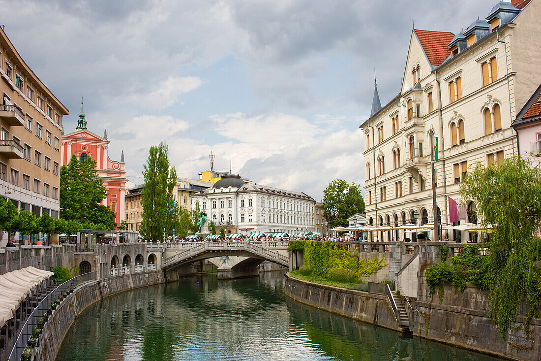 Ein Abschnitt des Flusses Ljubljanica, der zur Dreifachbrücke führt, die 1932 von Joze Plecnik entworfen wurde, und das Stadtzentrum, Ljubljana, Slowenien, Europa