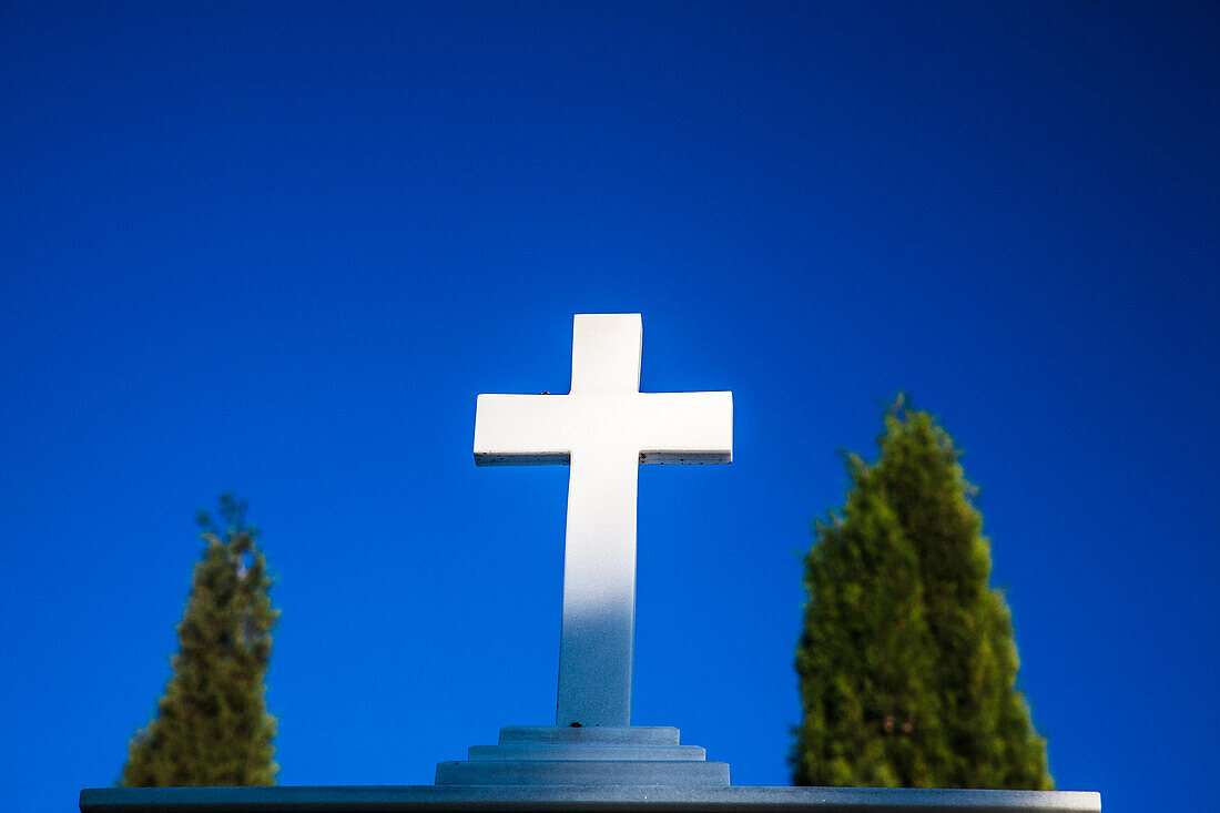 Weißes Kreuz auf dem katholischen Friedhof von Aznalcazar, Sevilla, Andalusien, Spanien, vor einem klaren blauen Himmel als Symbol für Glauben und Gelassenheit.