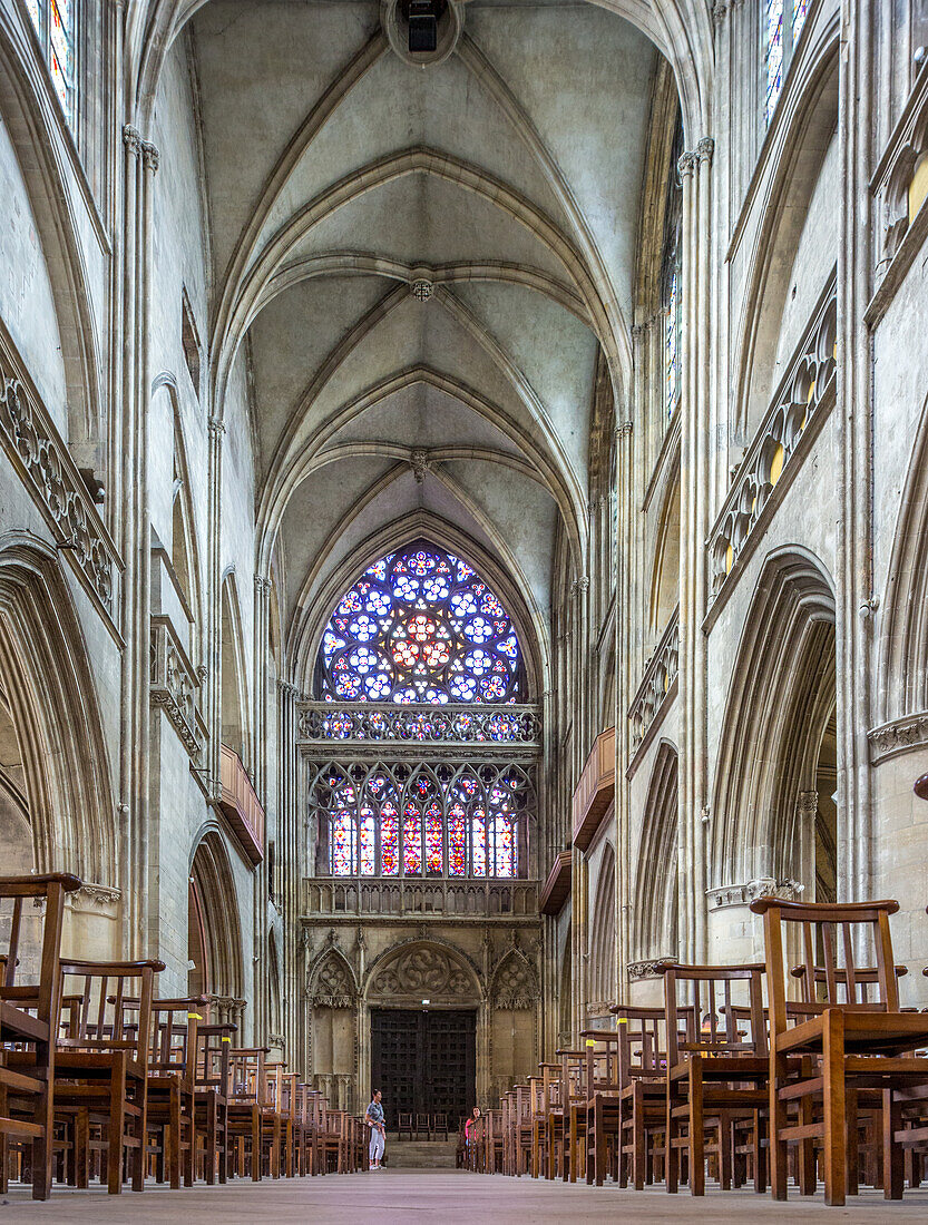 Innenansicht der Eglise Saint Pierre mit gotischer Architektur, Reihen von Holzstühlen und beeindruckenden Buntglasfenstern in Caen, Normandie, Frankreich.