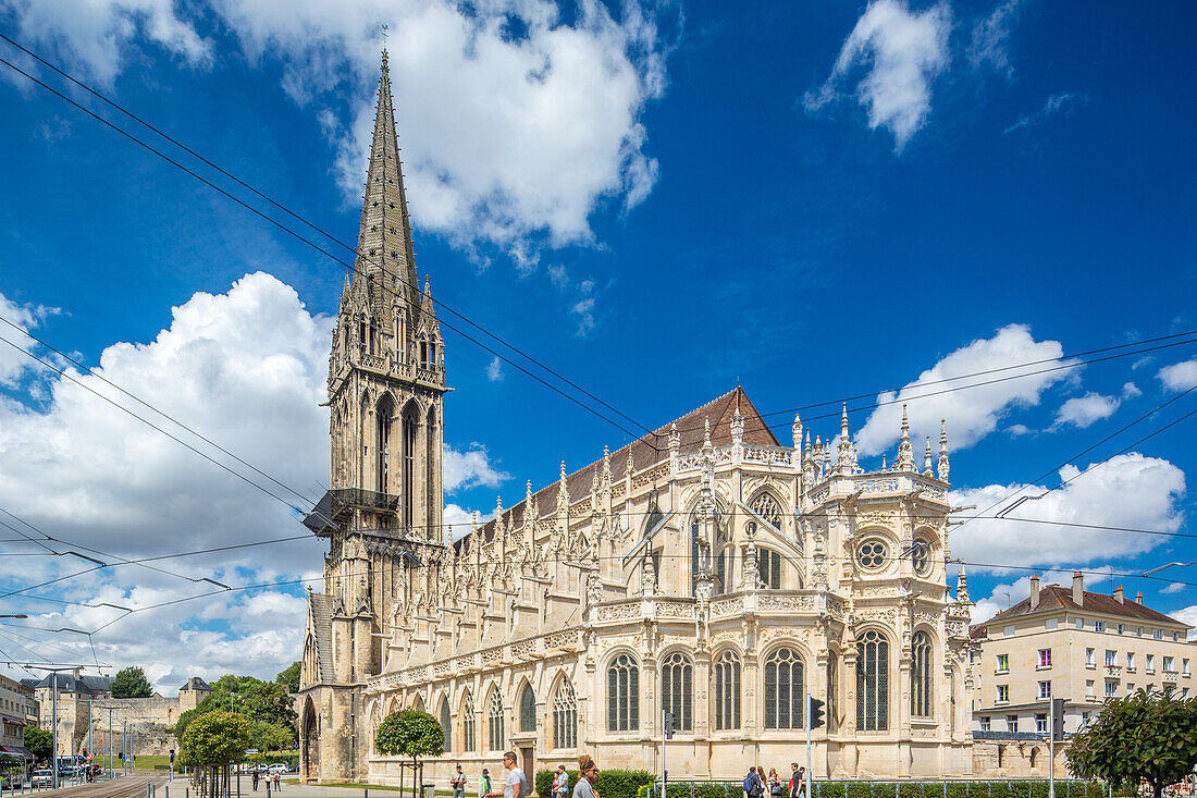 Stunning Gothic Church of Saint-Pierre, located in Caen, Normandy, France, with a bright blue sky and clouds. The architecture showcases detailed stonework and a tall spire.