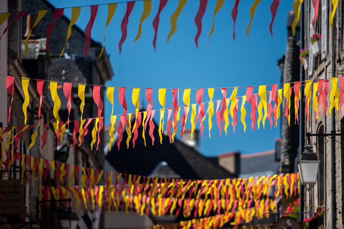 Vibrant red and yellow flags hanging across a charming street in Guerande, France on a sunny day.