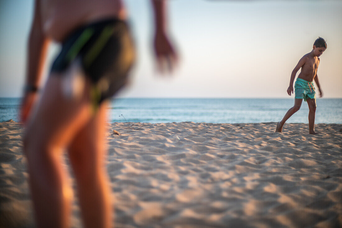 Children having fun and playing on the sandy shores of Zahora beach in Cadiz, Spain, with the sun setting over the ocean.