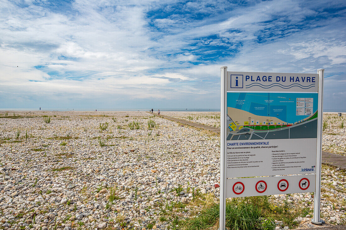 Weitwinkelansicht des felsigen Strandes Plage Du Havre in Le Havre, Frankreich, mit einem klaren Schild mit Strandhinweisen und einem teilweise bewölkten Himmel.