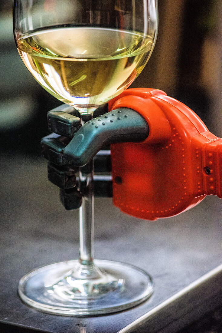 A close-up of a robot hand holding a glass of white wine, showcasing modern technology and relaxation.