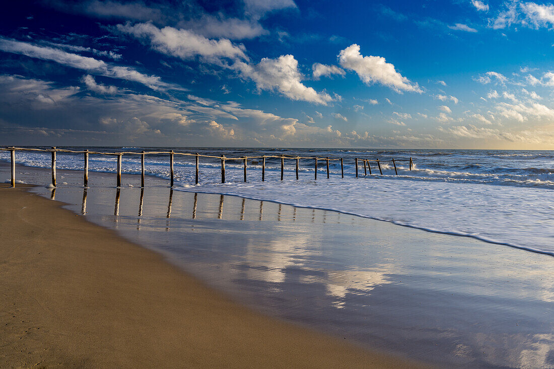 Ein Holzzaun, der die Grenze des Donana-Nationalparks am Strand von Matalascanas in Almonte, Huelva, Andalusien, Spanien, markiert, mit rauschenden Wellen und einem wunderschönen Himmel.