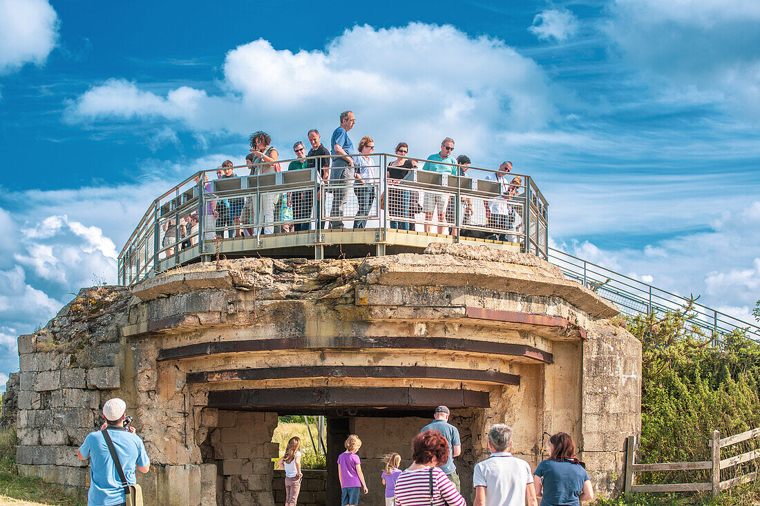 Group of tourists exploring a historic German bunker at Pointe du Hoc in Normandy, France. Scenic views and historic atmosphere.