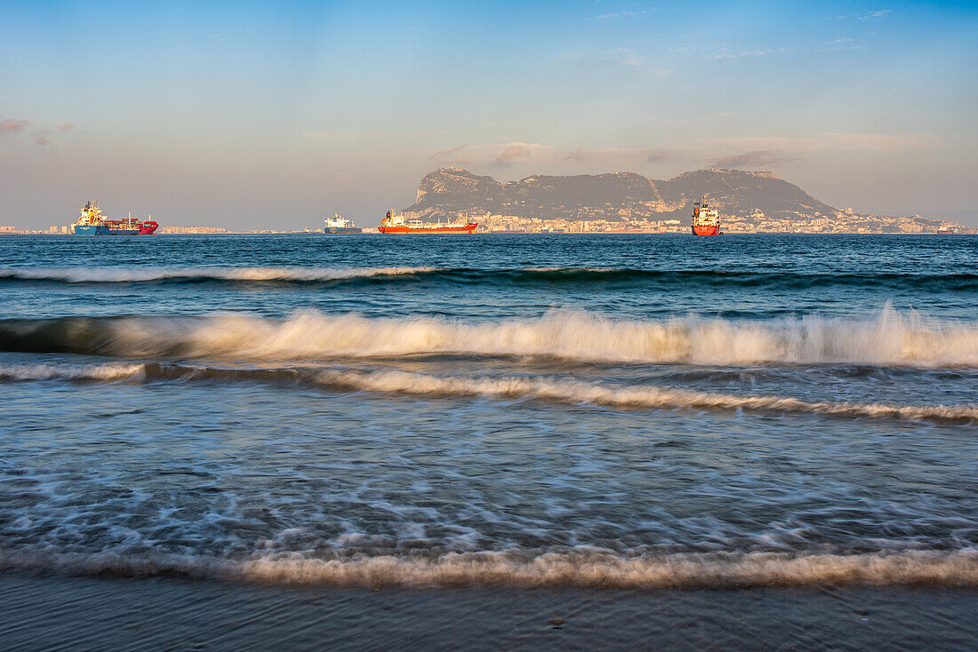 Gelassener Abend am Strand von El Rinconcillo, Algeciras, Spanien. Die Langzeitbelichtung fängt Frachtschiffe über der Bucht von Gibraltar in der Abenddämmerung ein.