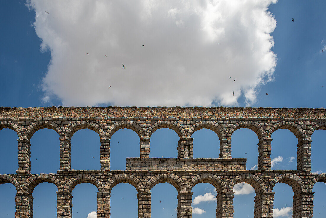 Historic Roman aqueduct in Segovia, Castilla y Leon, Spain. Featuring stone arches and a blue sky with clouds.