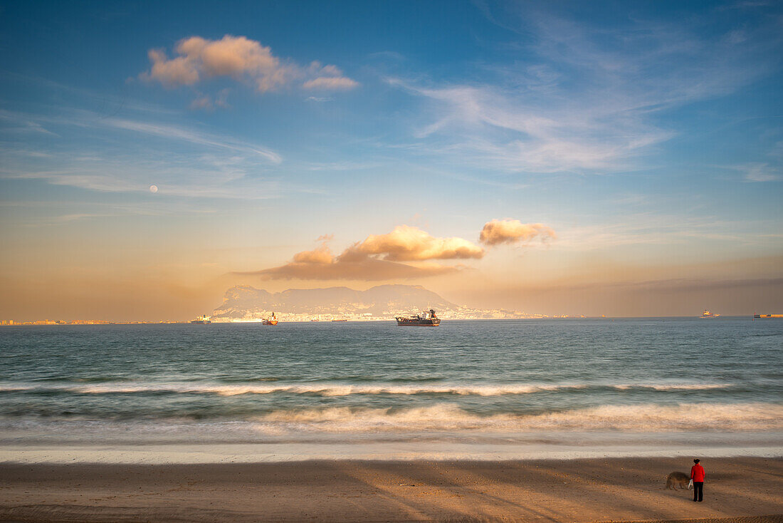 Beautiful beach scene at sunset with boats on the ocean and Gibraltar in the distance as seen from Algeciras, Spain.