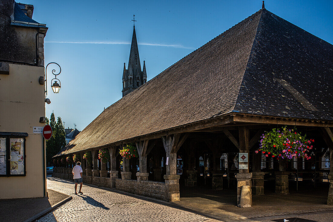 Blick bei Sonnenuntergang auf den historischen Marktplatz von Les Halles in Questembert, Bretagne, Frankreich. Mit Kopfsteinpflaster, Schatten und der Silhouette eines Kirchturms.