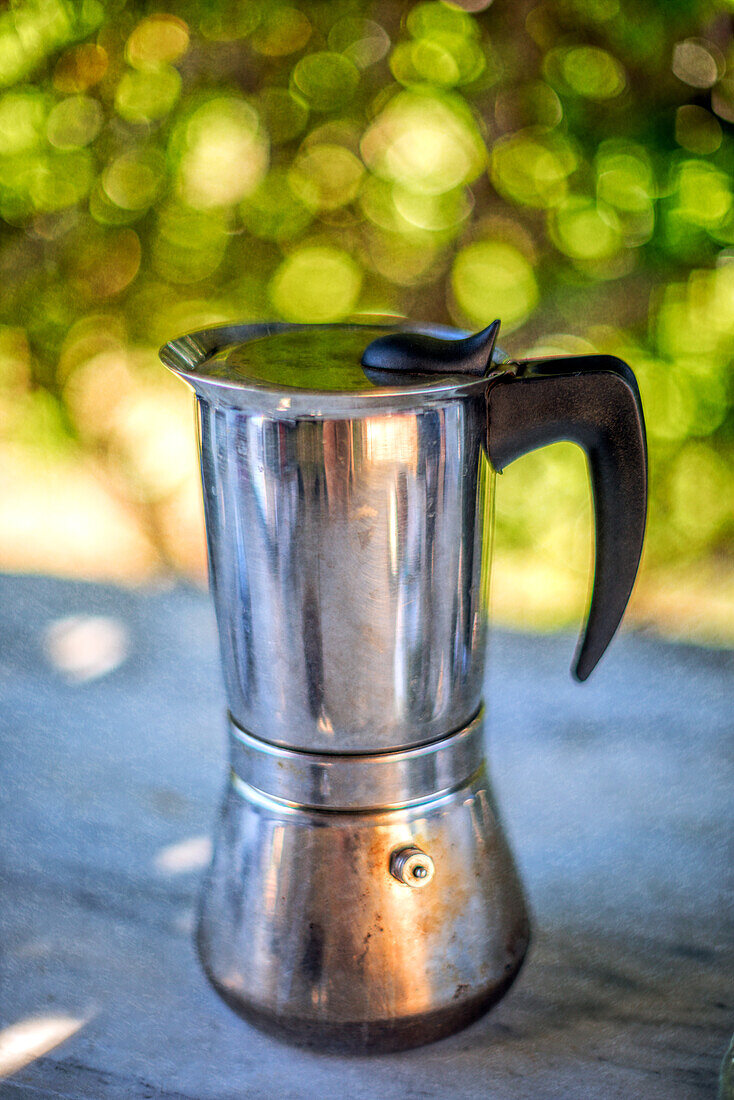 Kaffeemaschine aus Edelstahl auf einem sonnigen Tisch im Freien in Fuenteheridos, Huelva. Ein nostalgisches Bild vom Morgenkaffee.