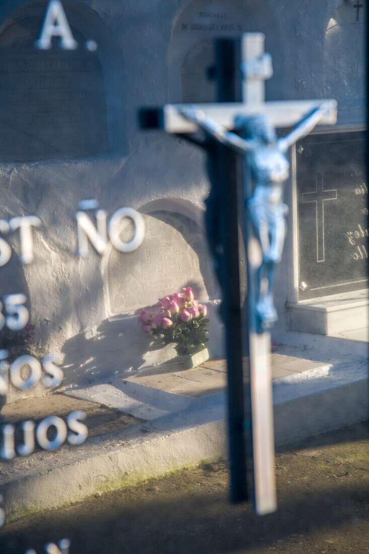 Nahaufnahme eines Kruzifixes und eines Grabsteins auf einem katholischen Friedhof in Aznalcazar, Provinz Sevilla, Andalusien, Spanien, der eine feierliche und respektvolle Atmosphäre widerspiegelt.