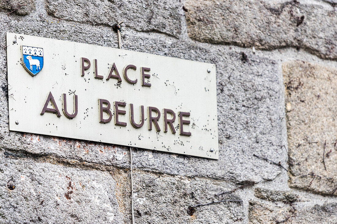 Nahaufnahme eines Straßenschilds am Place Au Beurre in Quimper, Bretagne, Frankreich. Steinmauer im Hintergrund und Wappen sichtbar.