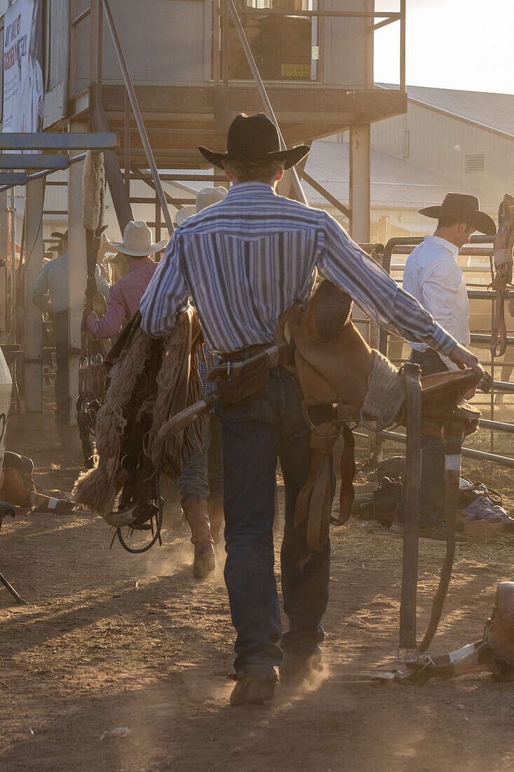 A saddle bronc cowboy carries his special bucking saddle to the bucking chutes at a rodeo in rural Utah.