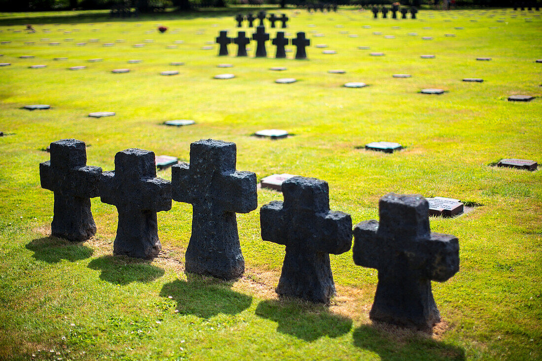 Eine friedliche Szene auf dem deutschen Soldatenfriedhof in der Normandie, Frankreich, mit Reihen von Steinkreuzen auf saftig grünem Gras.