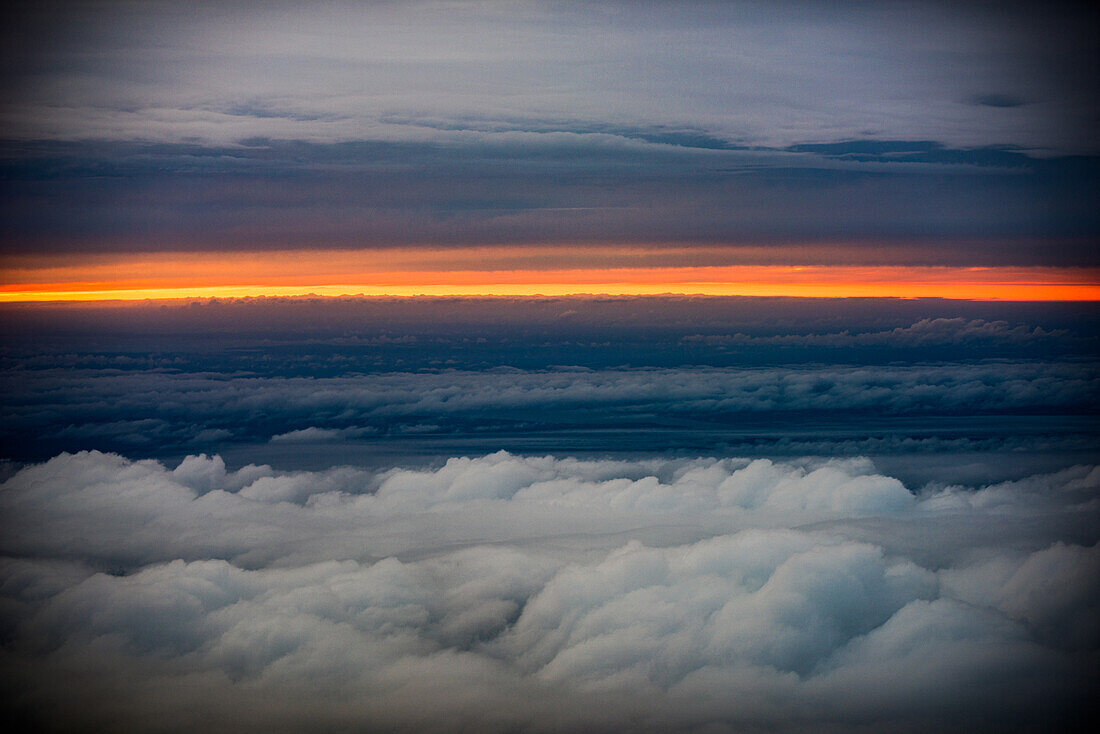 Atemberaubender Blick auf einen Sonnenuntergang aus einem Flugzeug über Frankreich, über einem Meer von Wolken, die den heiteren Himmel hervorheben.