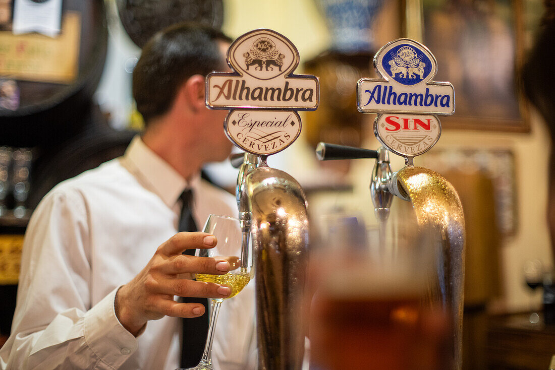 Ein Barkeeper schenkt Bier in einer traditionellen Bar in Granada, Andalusien, Spanien, aus. Die Szene fängt die lokale Kultur und den Genuss feiner Getränke ein.