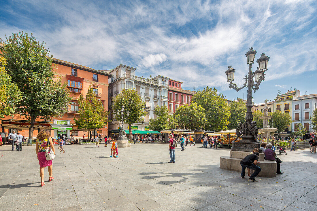 Bustling scene in Plaza de Bib Rambla, Granada, Spain, with people enjoying a sunny day surrounded by historic buildings.