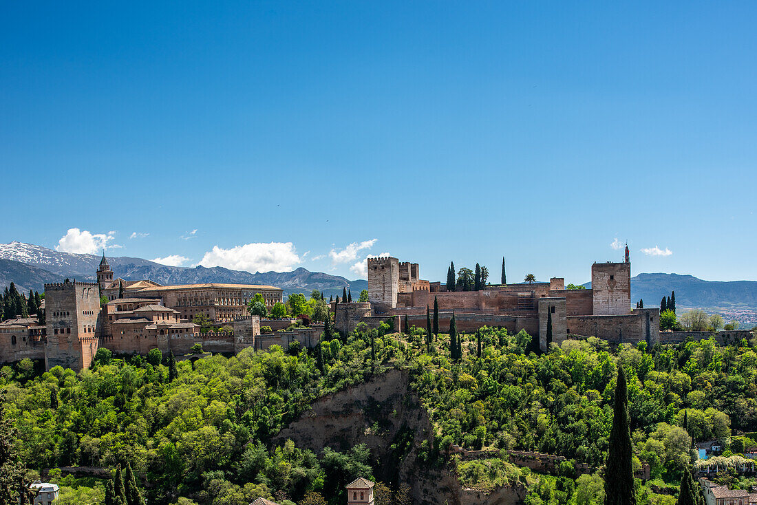 Scenic view of La Alhambra from Albaycin, Granada, Spain, showcasing its historic architecture surrounded by lush greenery and distant mountains.