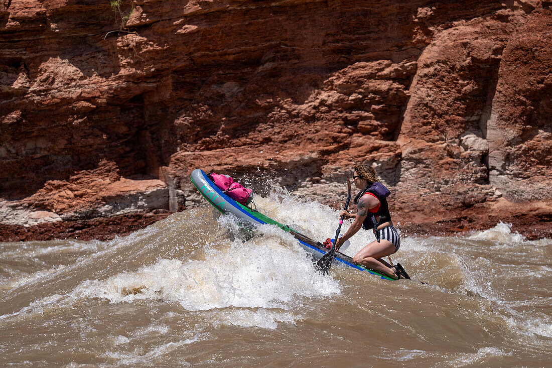 Eine junge Frau paddelt auf dem Wildwasser des White's Rapid auf dem Colorado River in der Nähe von Moab, Utah.