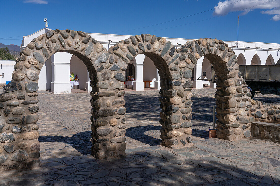 Steinbögen auf der Plaza 9 de julio, dem Stadtplatz in Cachi, Argentinien. Dahinter befinden sich die Bögen des Arqueologischen Museums Pio Pablo Diaz.