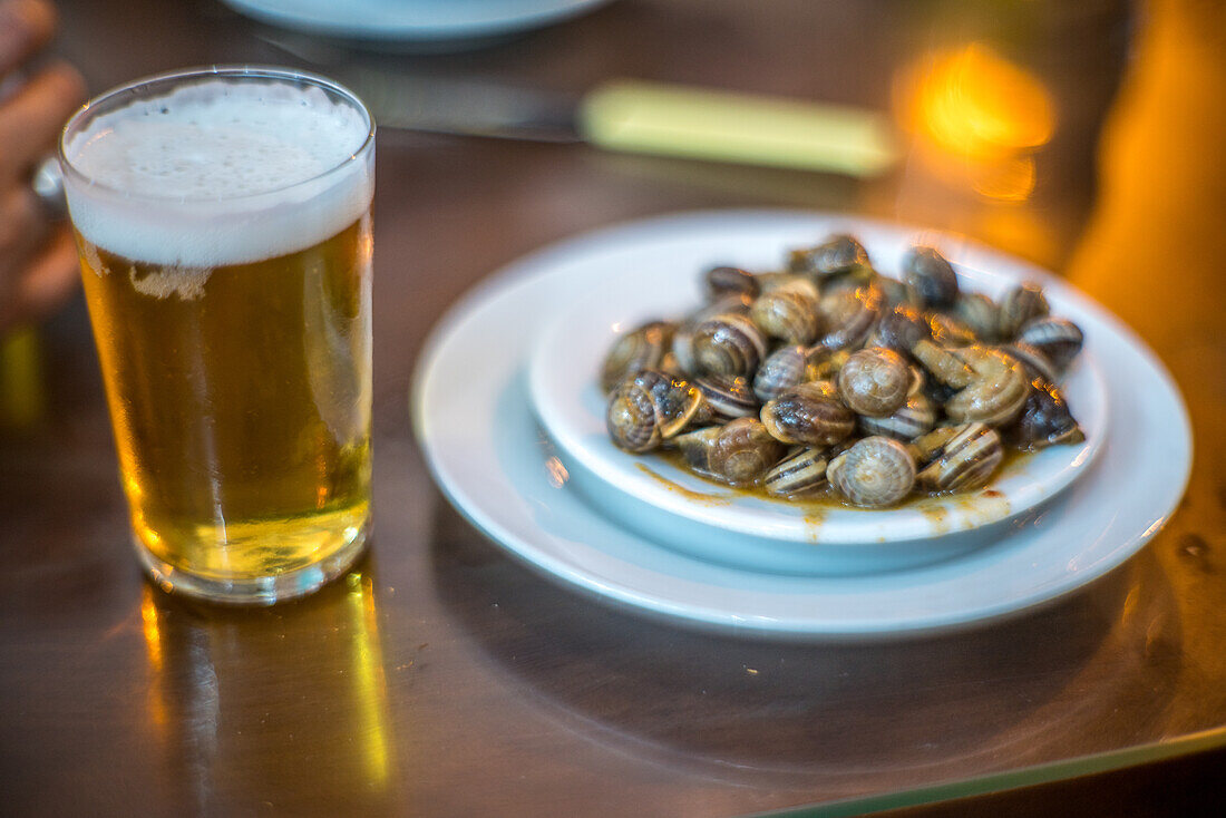 A glass of beer and a plate of Andalusian-style snails, a typical tapas dish, served in a Seville tavern.