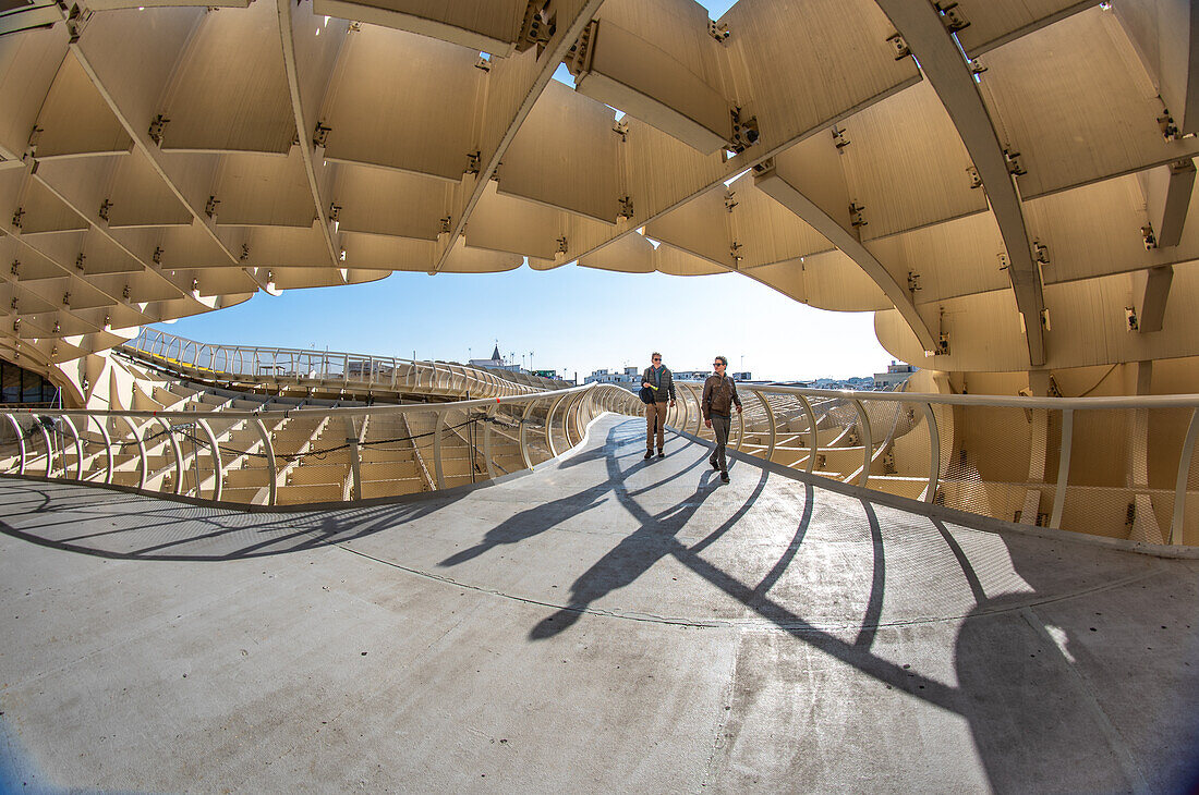 Two people walking on the iconic Las Setas structure in Seville, Andalusia, Spain, under a clear blue sky.