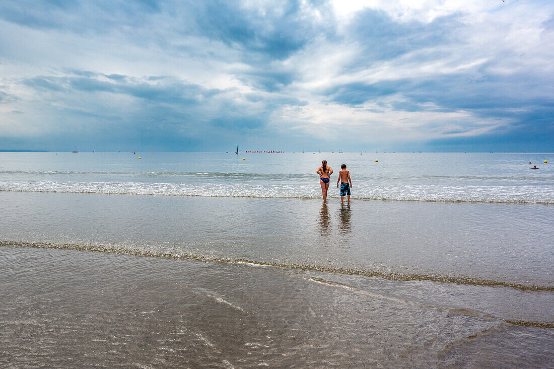 Two children are seen enjoying their time at the beach in Le Havre, France, under a cloudy sky.