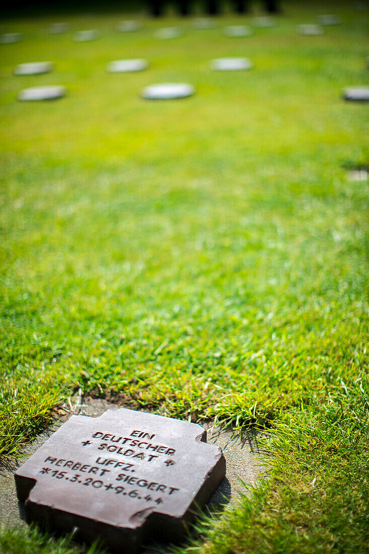 Close-up view of a gravestone at the German military cemetery in Normandy, France. Memorial site for fallen soldiers with a peaceful green landscape.