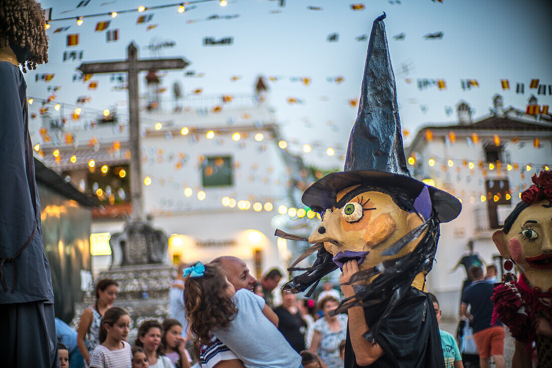 Ein lebhaftes Fest in Fuenteheridos, Huelva, mit der traditionellen Parade Gigantes y Cabezudos. Familien versammeln sich, um die Festlichkeiten und bunten Kostüme zu genießen.