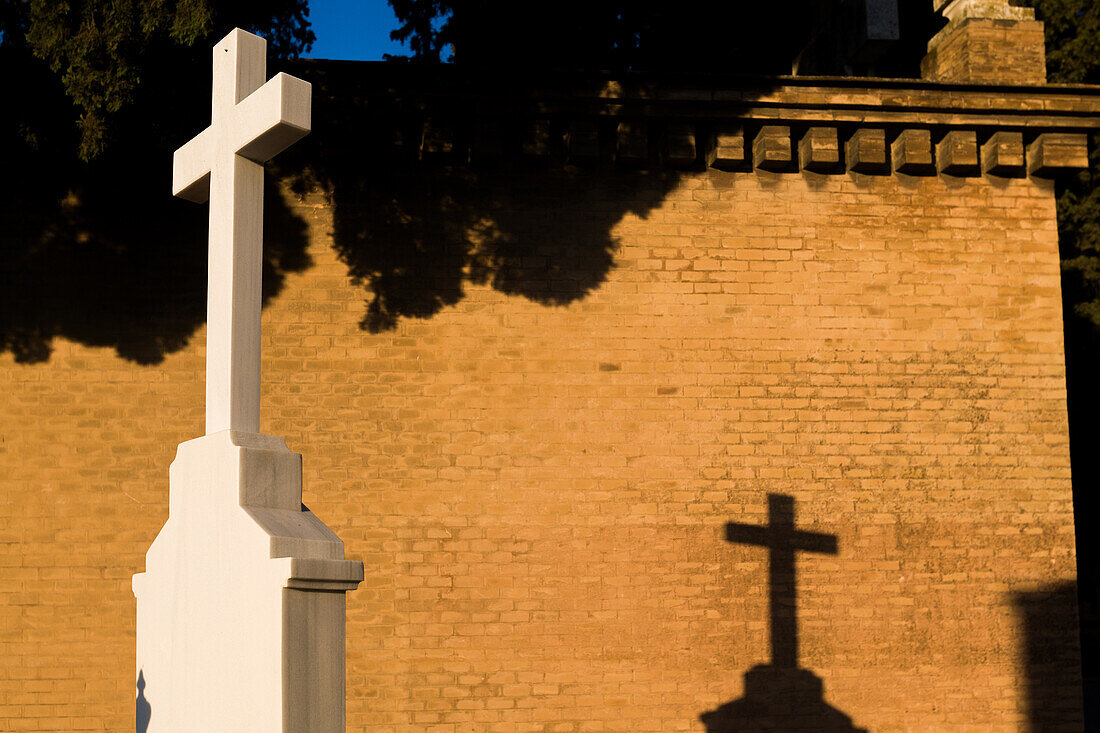 White cross casting a shadow on a brick wall at Cementerio de San Fernando in Sevilla, Andalucia during sunset.