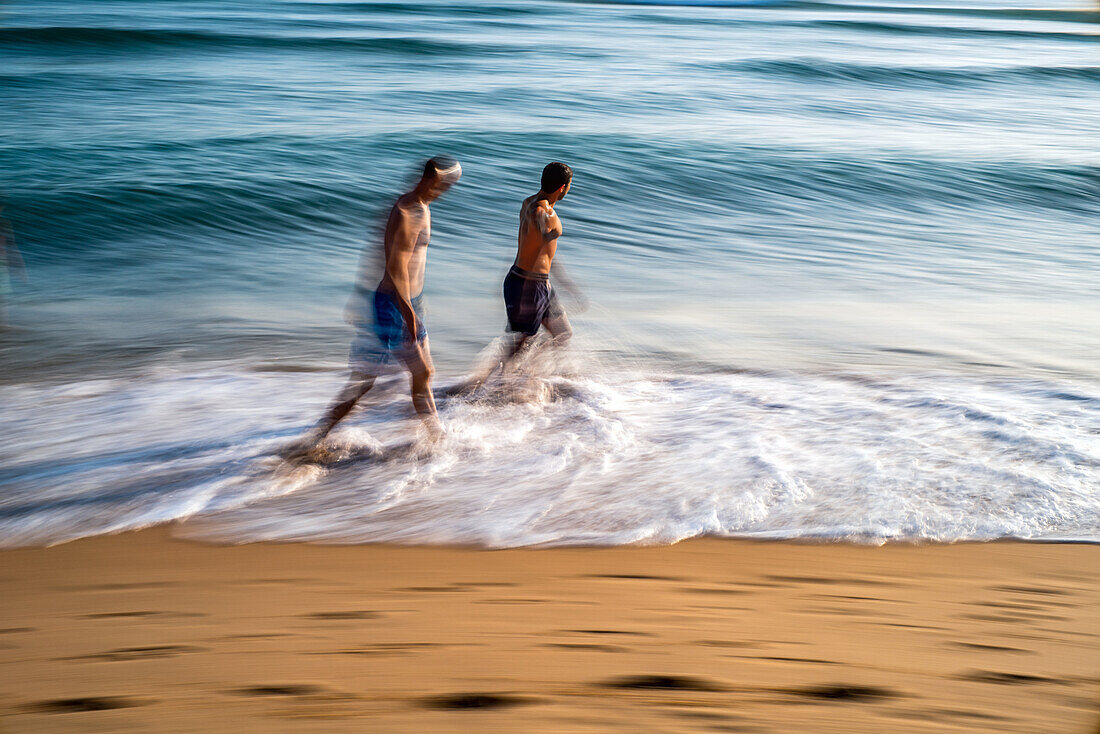 Langzeitbelichtung von Menschen, die am Strand von Zahora in Cádiz, Spanien, spazieren gehen, mit bewegten Wellen.