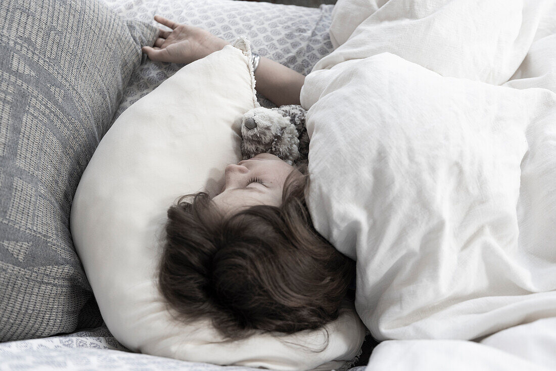 Blick von oben auf einen Jungen, der mit einem Kuscheltier im Bett schläft