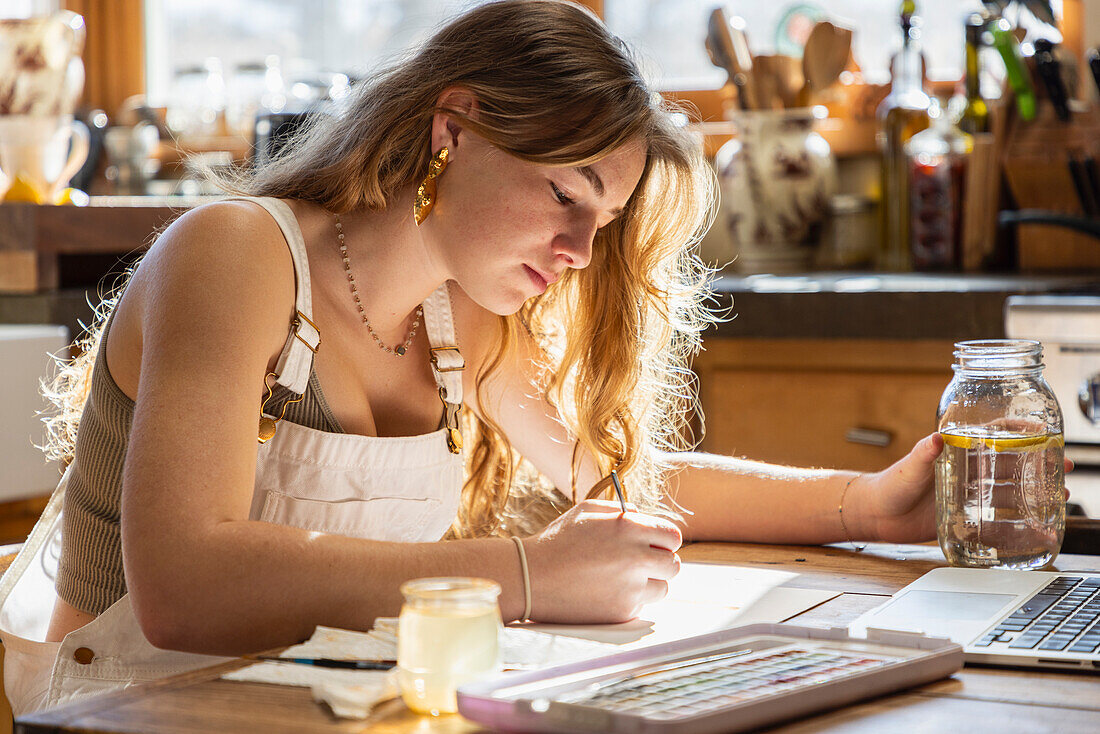 Teenagerin malt mit Aquarellfarben am Tisch