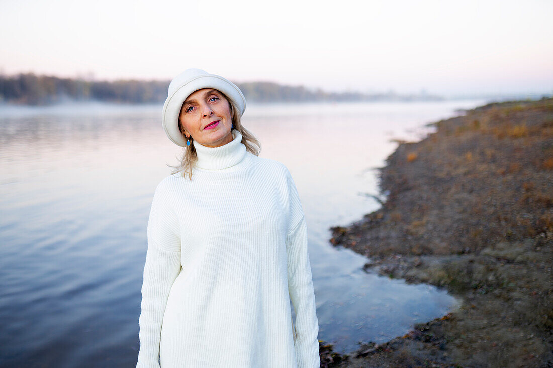 Porträt einer Frau mit weißem Hut und Pullover am Seeufer