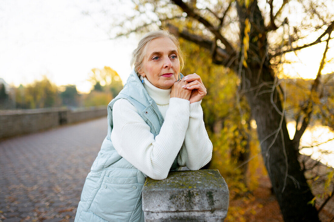 Porträt einer Frau, die sich im Herbst an eine Mauer am Fluss lehnt