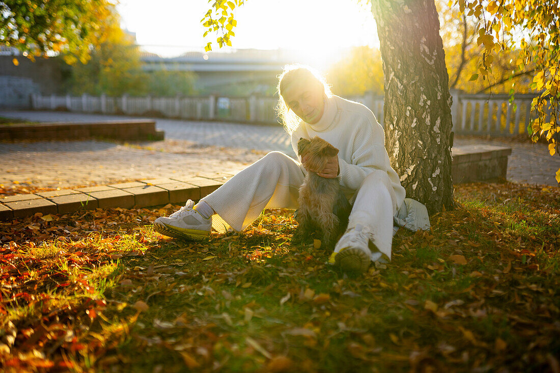 Frau mit Yorkshire Terrier sitzt im Herbst auf einer Wiese