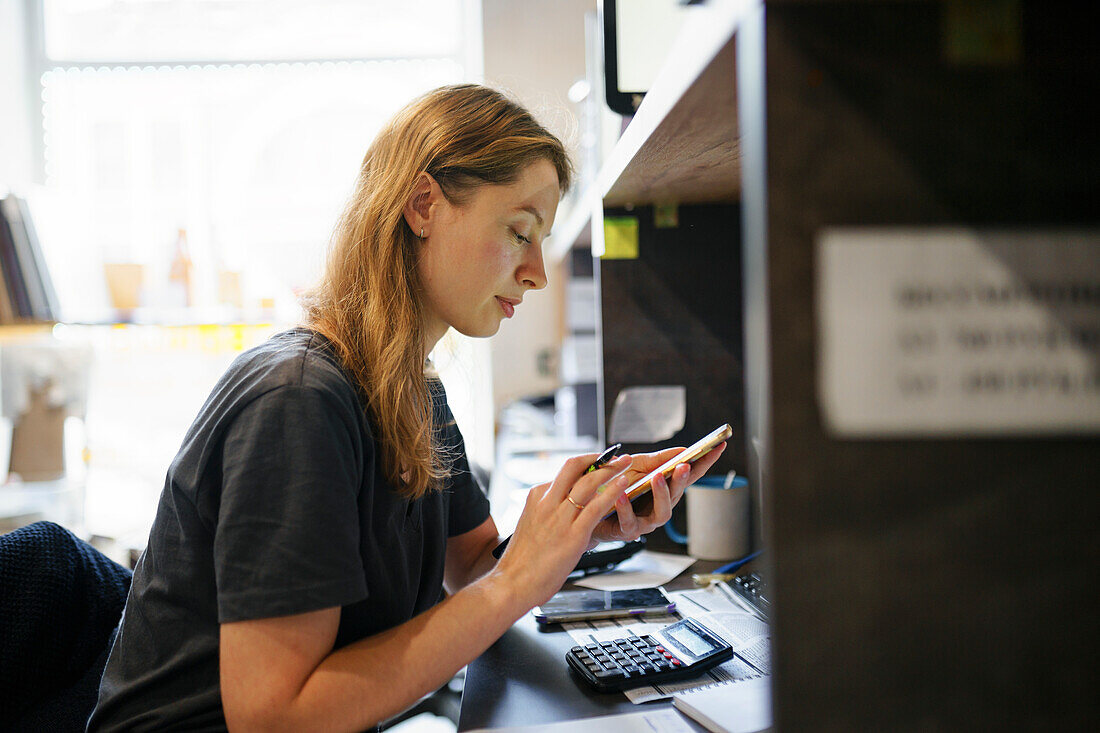 Frau schaut auf ihr Smartphone am Schreibtisch im Büro