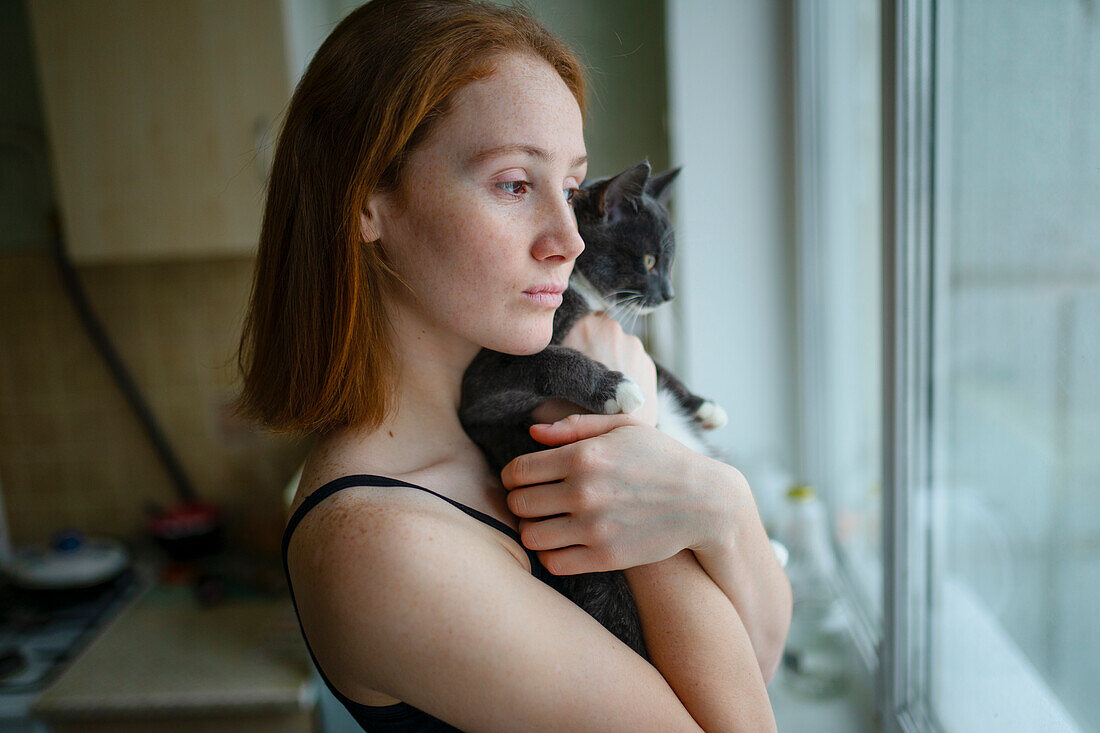 Nachdenkliche Frau mit Katze schaut durch ein Fenster