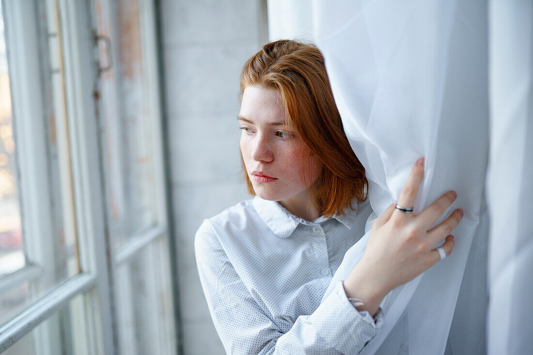 Porträt einer nachdenklichen Frau, die durch ein Fenster schaut