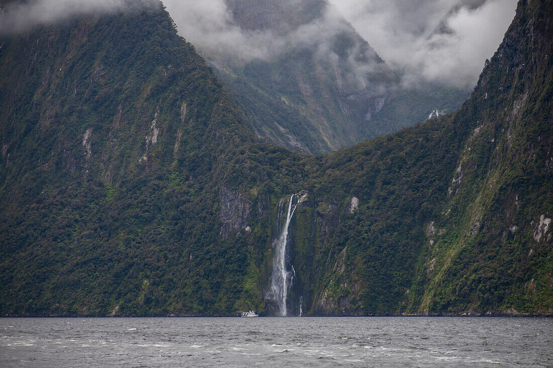 Fähre auf einem Fjord in der Nähe eines Wasserfalls im Fiordland-Nationalpark