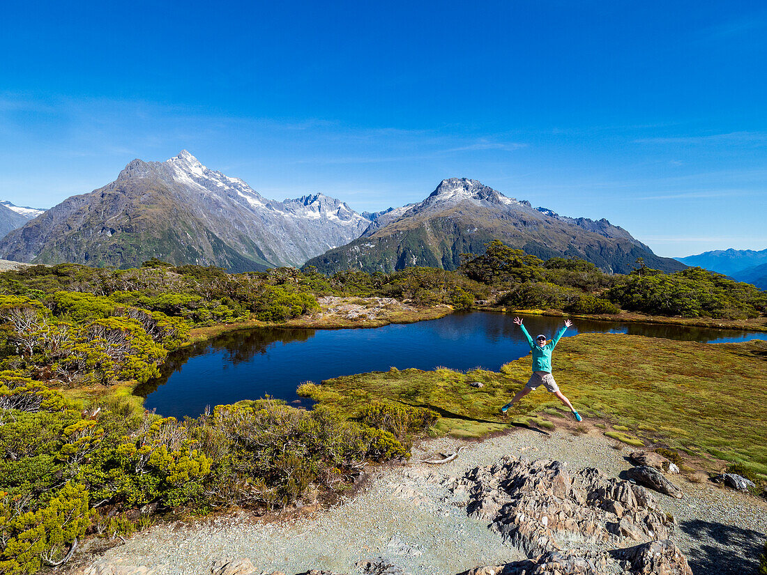 Frau springt in Landschaft im Fiordland-Nationalpark