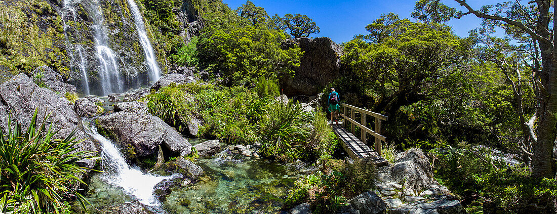 Rückansicht eines Wanderers, der einen Steg in der Nähe eines Wasserfalls im Fiordland-Nationalpark überquert