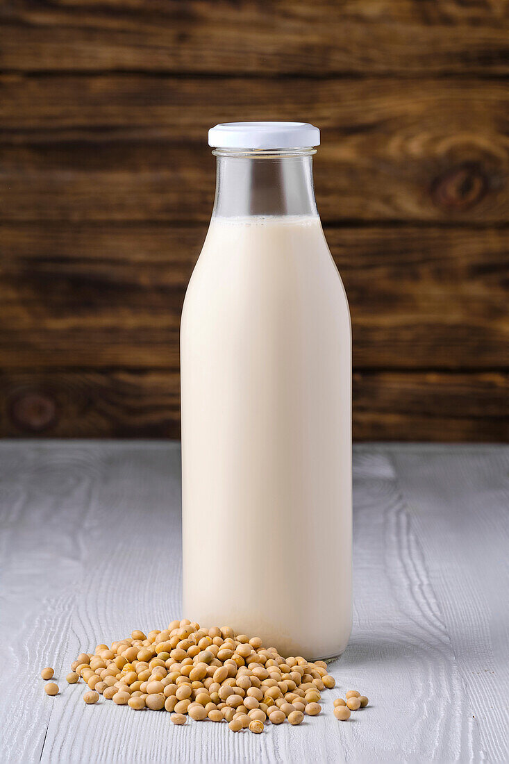 Bottle of soy milk with soybeans on a wooden base