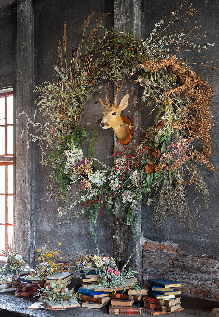 Large autumn wreath of dried flowers, deer head in the centre, stack of books underneath