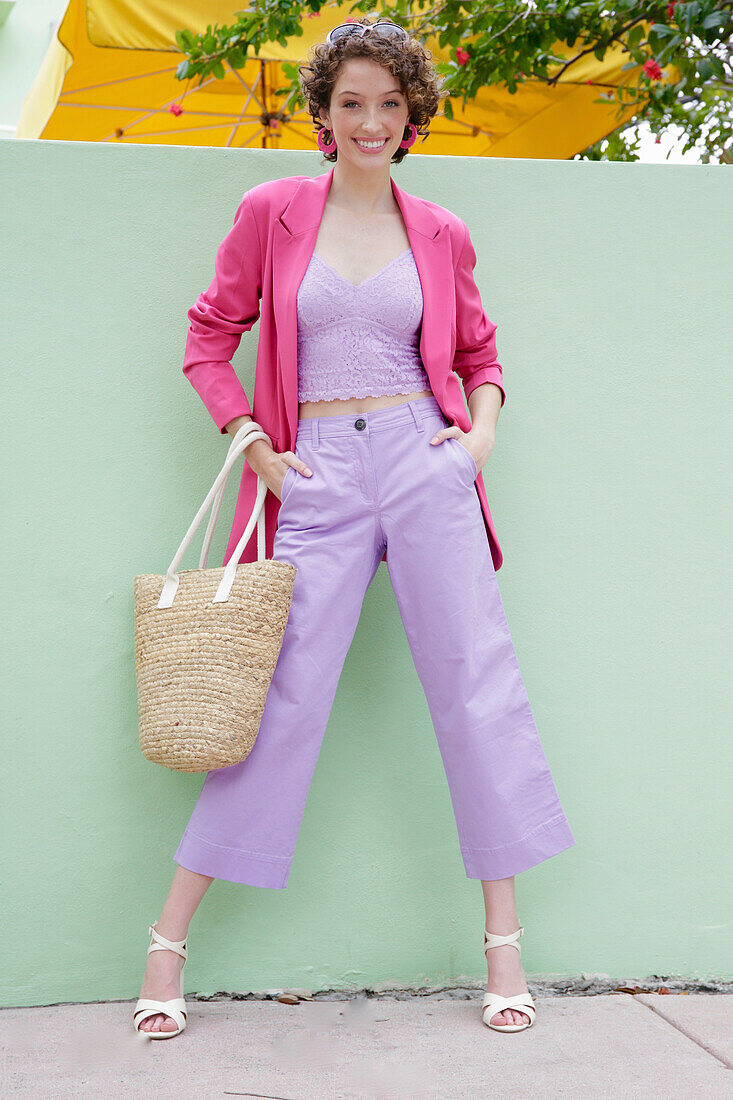 Young woman in lavender-coloured suit with pink blazer in front of mint-green building